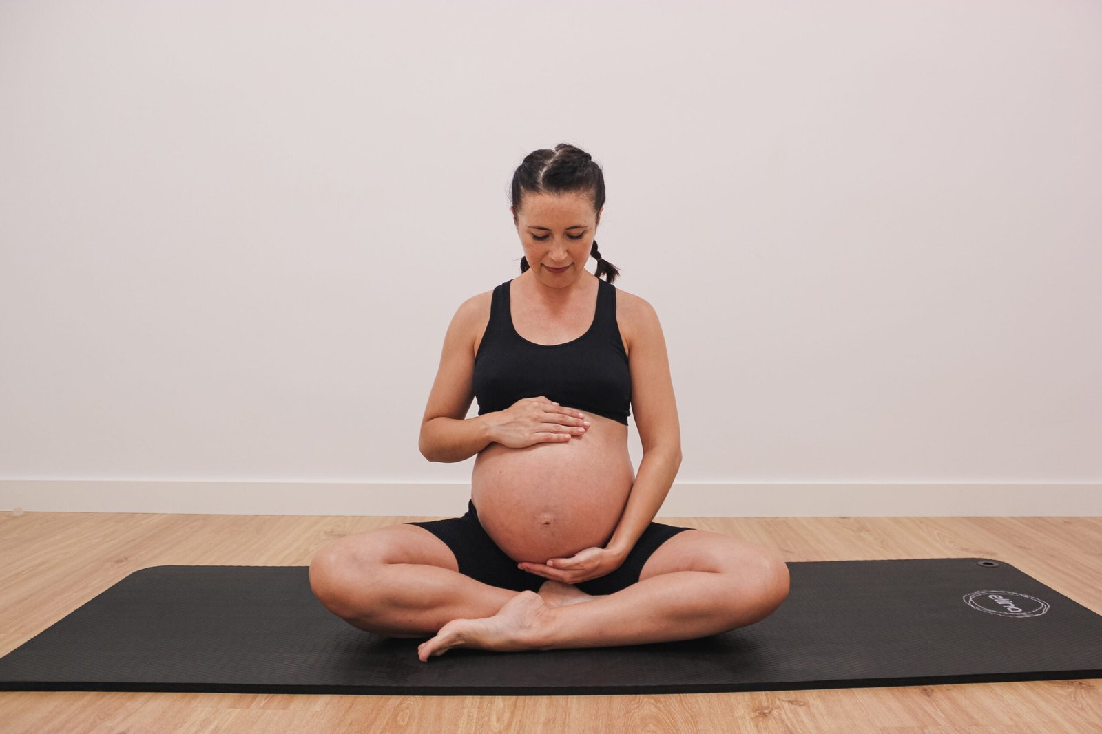 Paciente embarazada enseñando la barriga y sentada en una colchoneta de pilates.