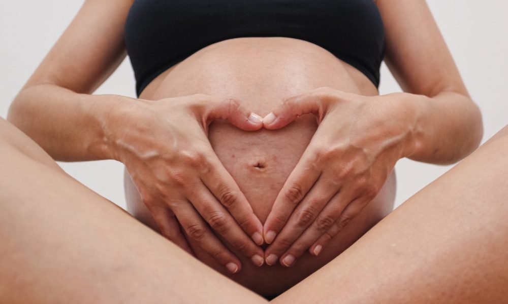 Paciente embarazada enseñando la barriga y haciendo la forma de un corazón con sus manos.